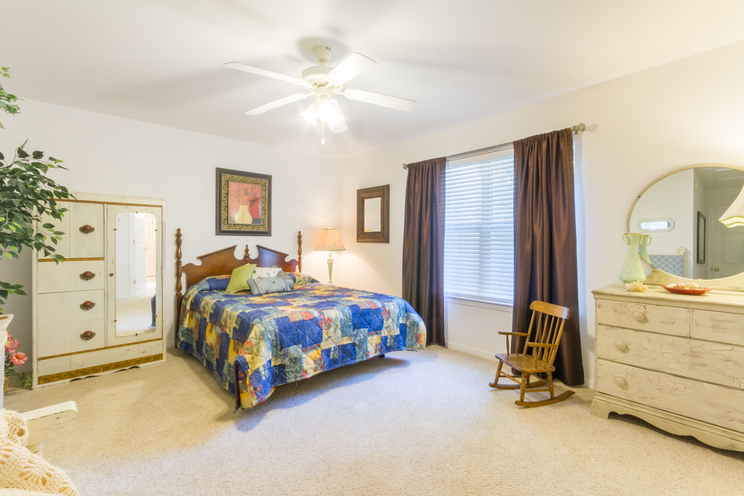 Une chambre à coucher comprenant un lit, une commode, une chaise et un ventilateur de plafond.