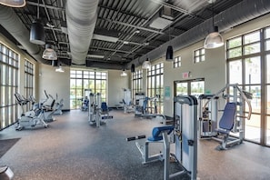 A gym with various exercise equipment, large windows, and an exit sign.