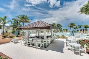A covered outdoor seating area with a pool in the background.