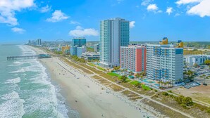 A coastal cityscape with a beach, high-rise buildings, and a pier. - Atlantica 1055 (Myrtle Beach)