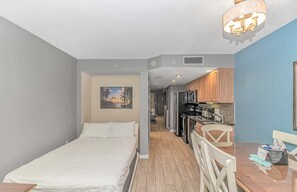 A bedroom with a bed, a kitchenette with a refrigerator, and a dining area with a table and chairs.