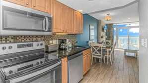 A kitchen with wooden cabinets, a microwave, stove, and dishwasher, leading to a balcony with a view. - Atlantica 1055 (Myrtle Beach)