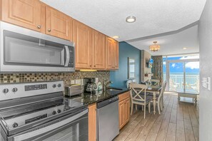 A kitchen with wooden cabinets, a microwave, stove, and dishwasher, leading to a balcony with a view.
