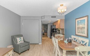 A compact living space with a dining area, kitchenette, and a hallway leading to another room.