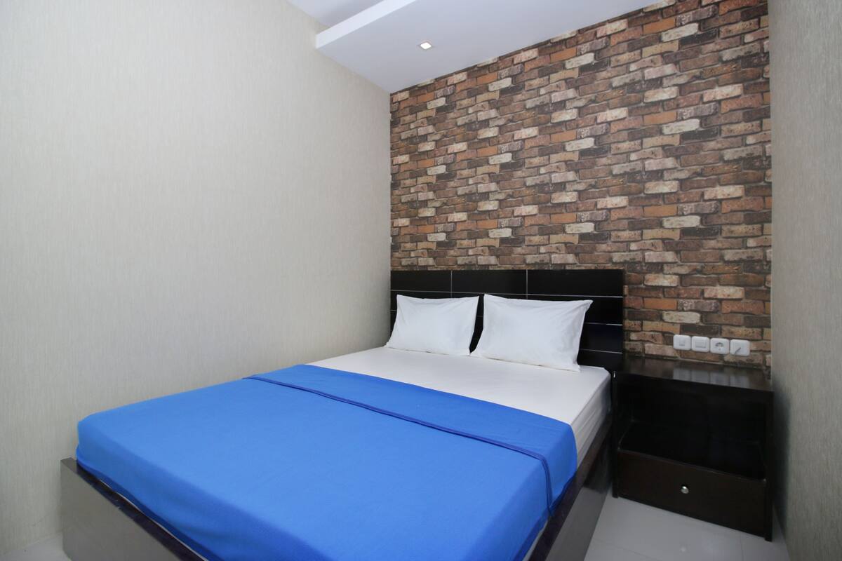 A bedroom with a brick-patterned wall, a bed with white and blue bedding, and a dark wooden nightstand.