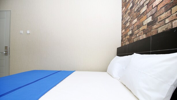A bed with white sheets and a blue blanket, a brick-patterned wall, and a door with a handle. - Kamar Keluarga Kampung Bali III Syariah (Jakarta)