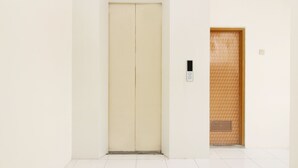 A plain white elevator with a simple control panel and a wooden door with a patterned design. - Kamar Keluarga Kampung Bali III Syariah (Jakarta)