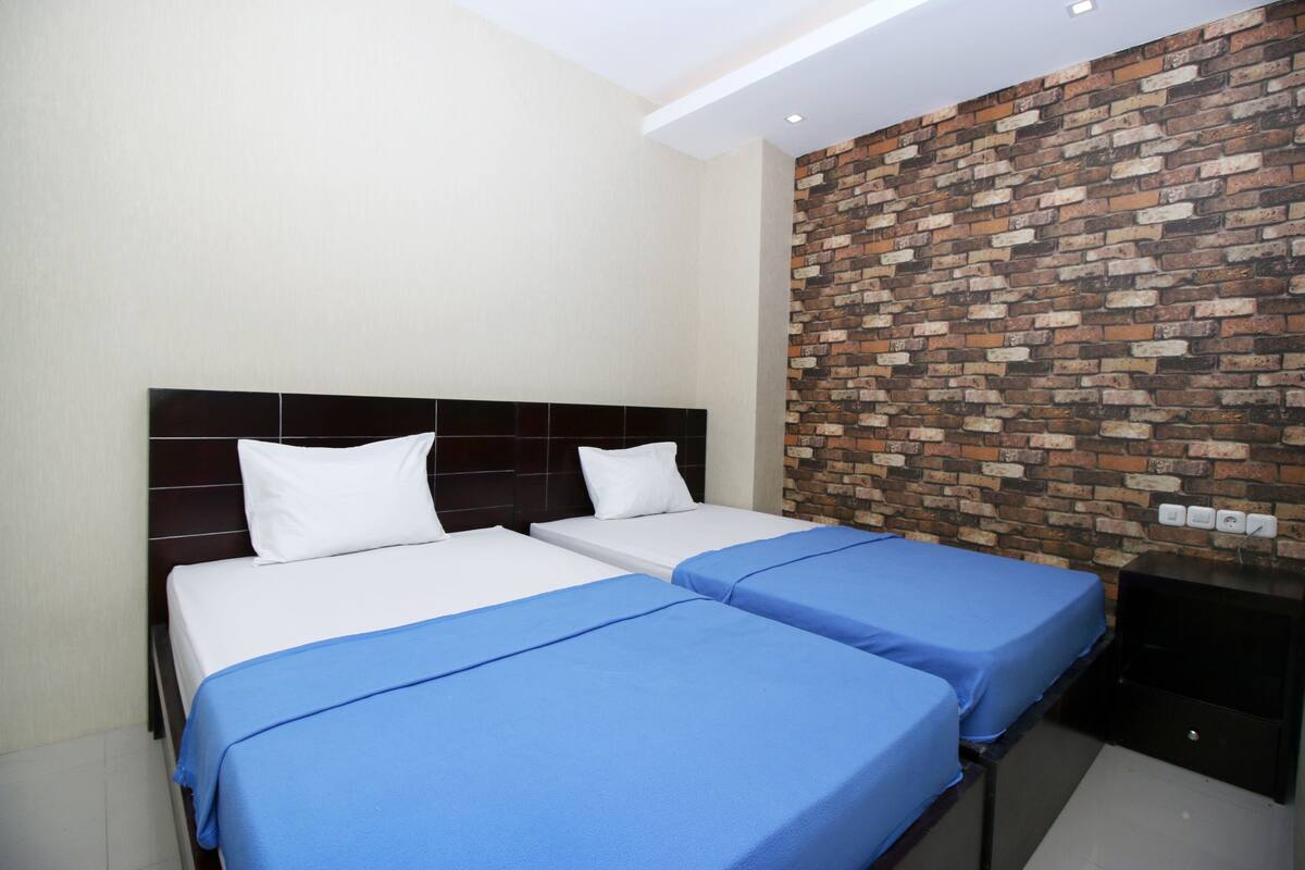 A hotel room with two beds, a brick wall, and a modern headboard.