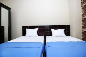 Una habitación de hotel con dos camas individuales, cada una con un almohadón blanco y una colcha azul. La habitación tiene una pared de ladrillo decorativa y un cabecero negro moderno.