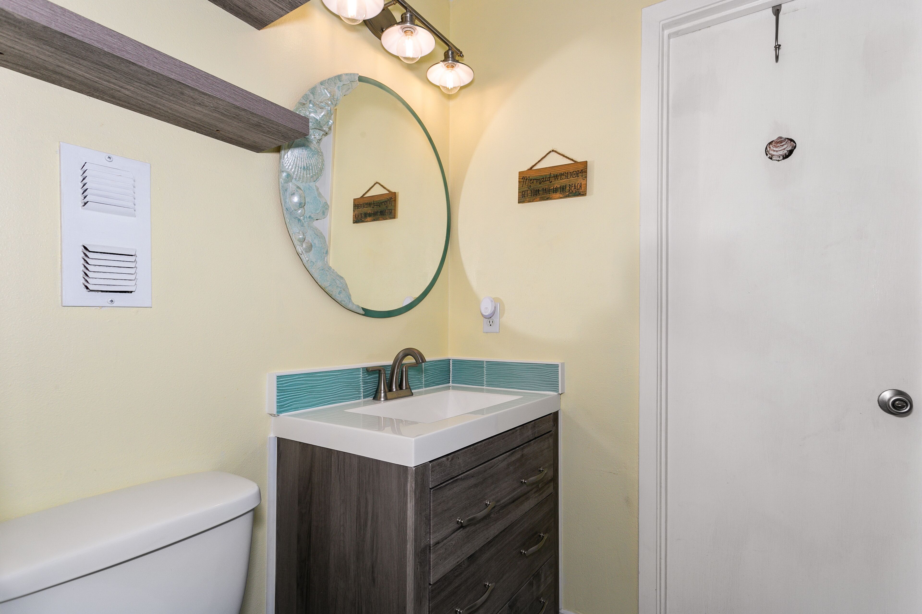 Un bagno con un water bianco, un lavabo con schienale verde acqua, un mobile bagno in legno scuro, uno specchio in vetro e un lampadario sopra lo specchio.