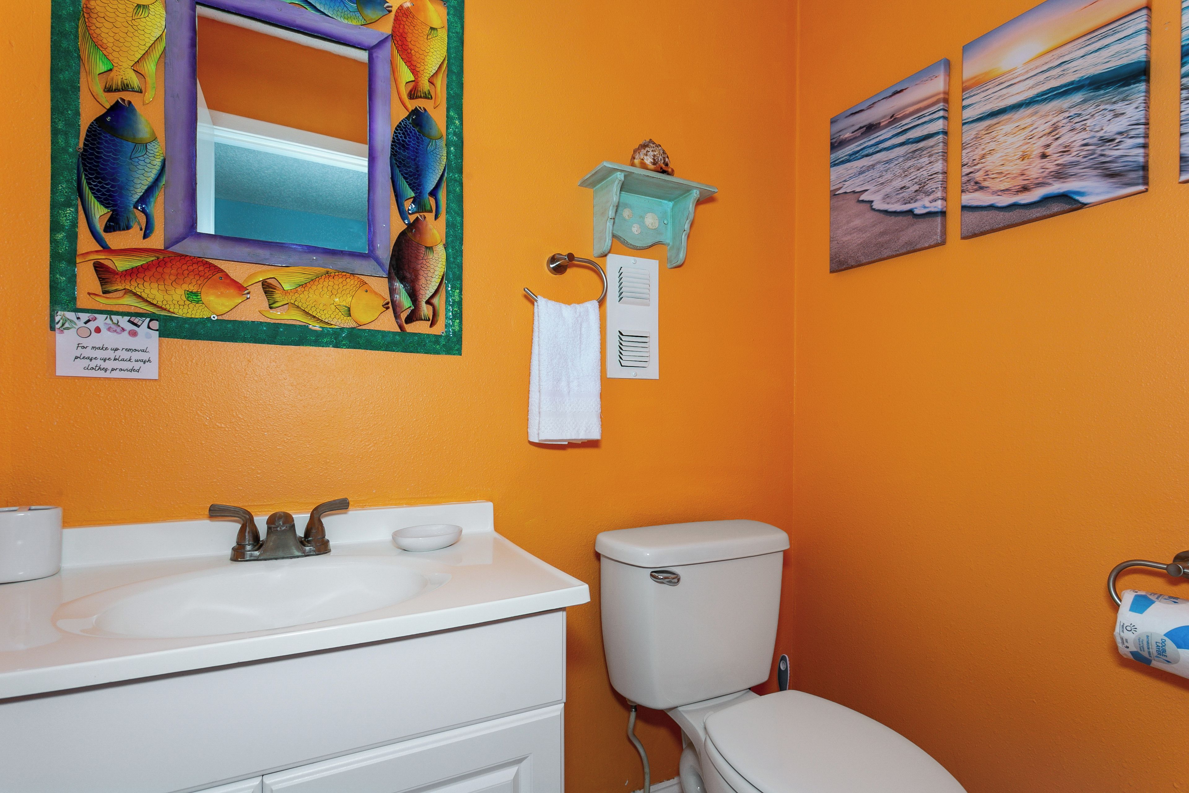 A bathroom with an orange wall, a white sink, a toilet, and decorative fish artwork.