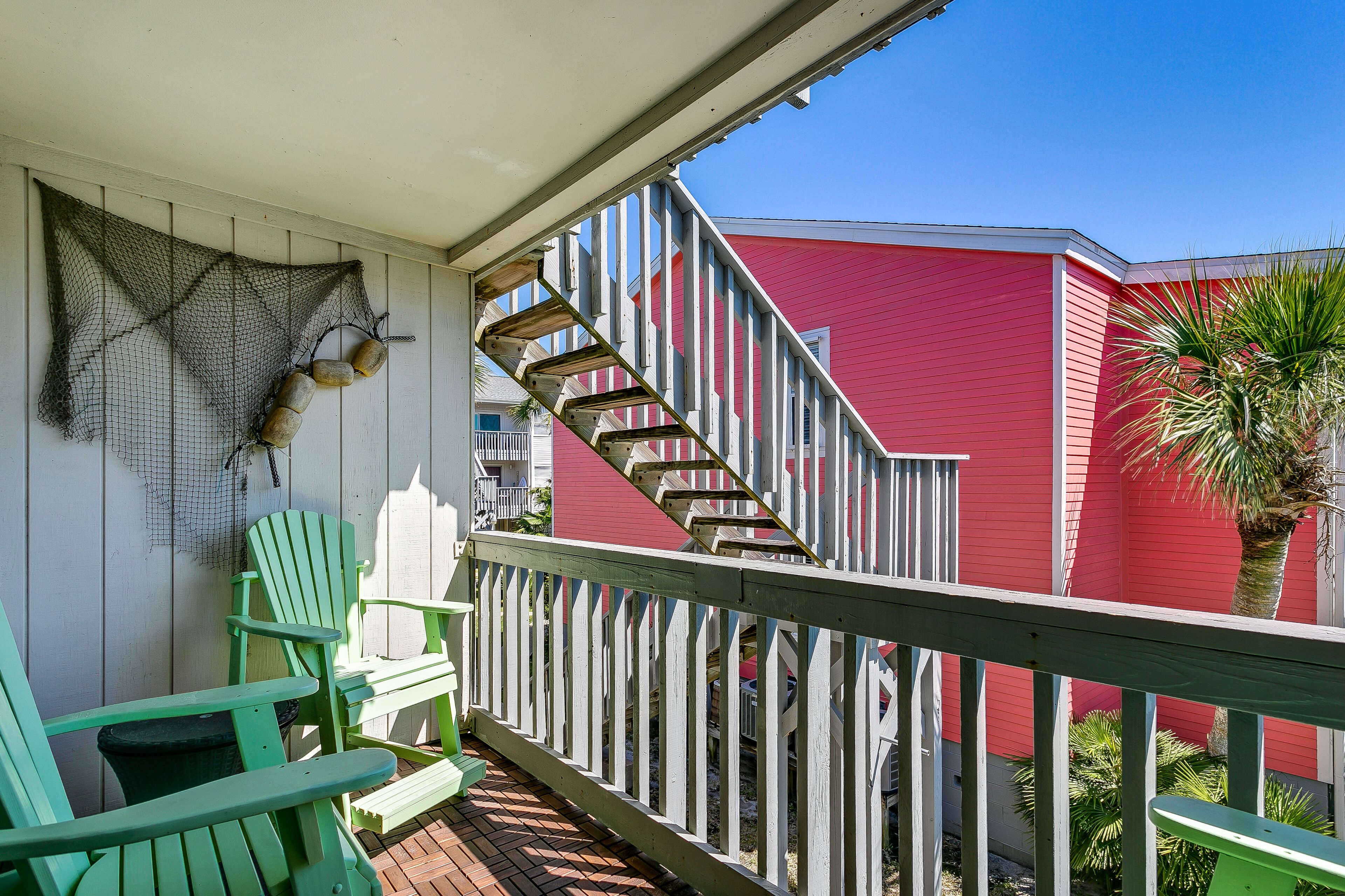 A balcony with green chairs, a white railing, and a red building in the background.