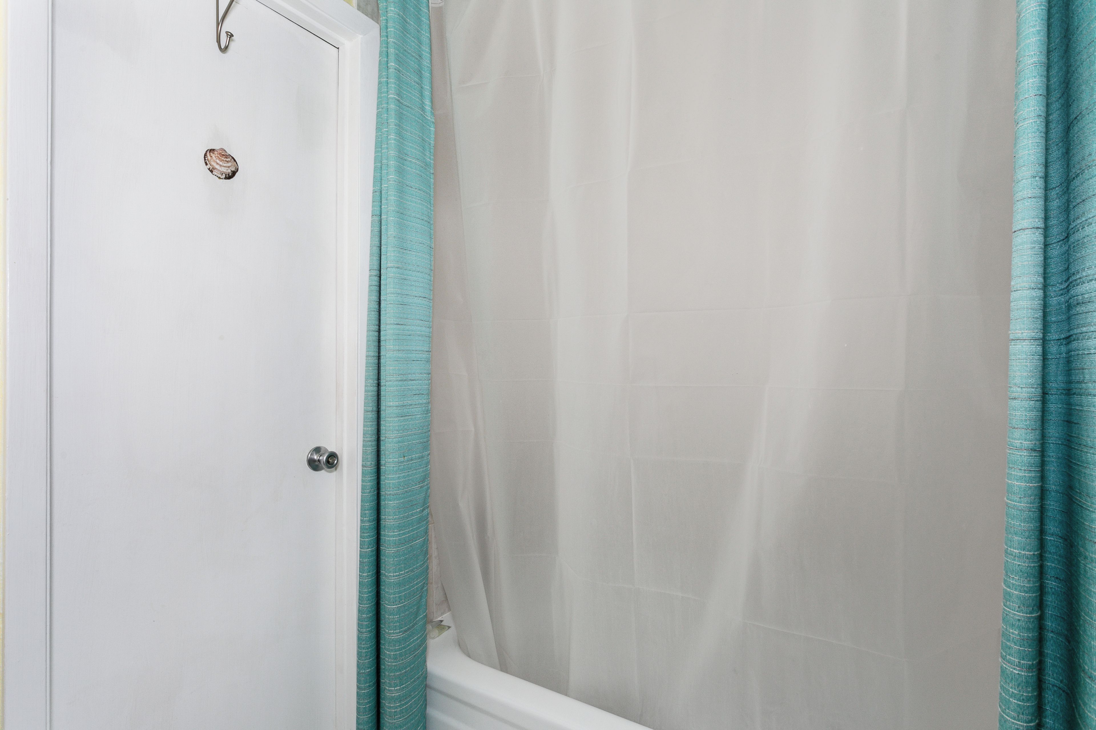 Een badkamer met een witte deur, douchegordijn en een bad.
