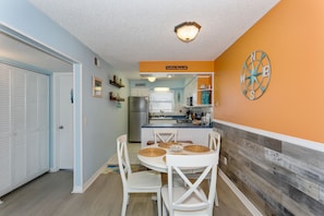 Cocina compacta con zona de comedor, que incluye una isla central, sillas blancas y un adorno de brújula en la pared.