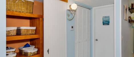 A hallway with a wooden shelf unit containing baskets and books, a white door with a light fixture above it, and a sign on the door.