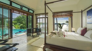A spacious bedroom with a four-poster bed, large windows, and a view of a pool and greenery. - Luxury Beach Front Noble House Villa (Wichit)