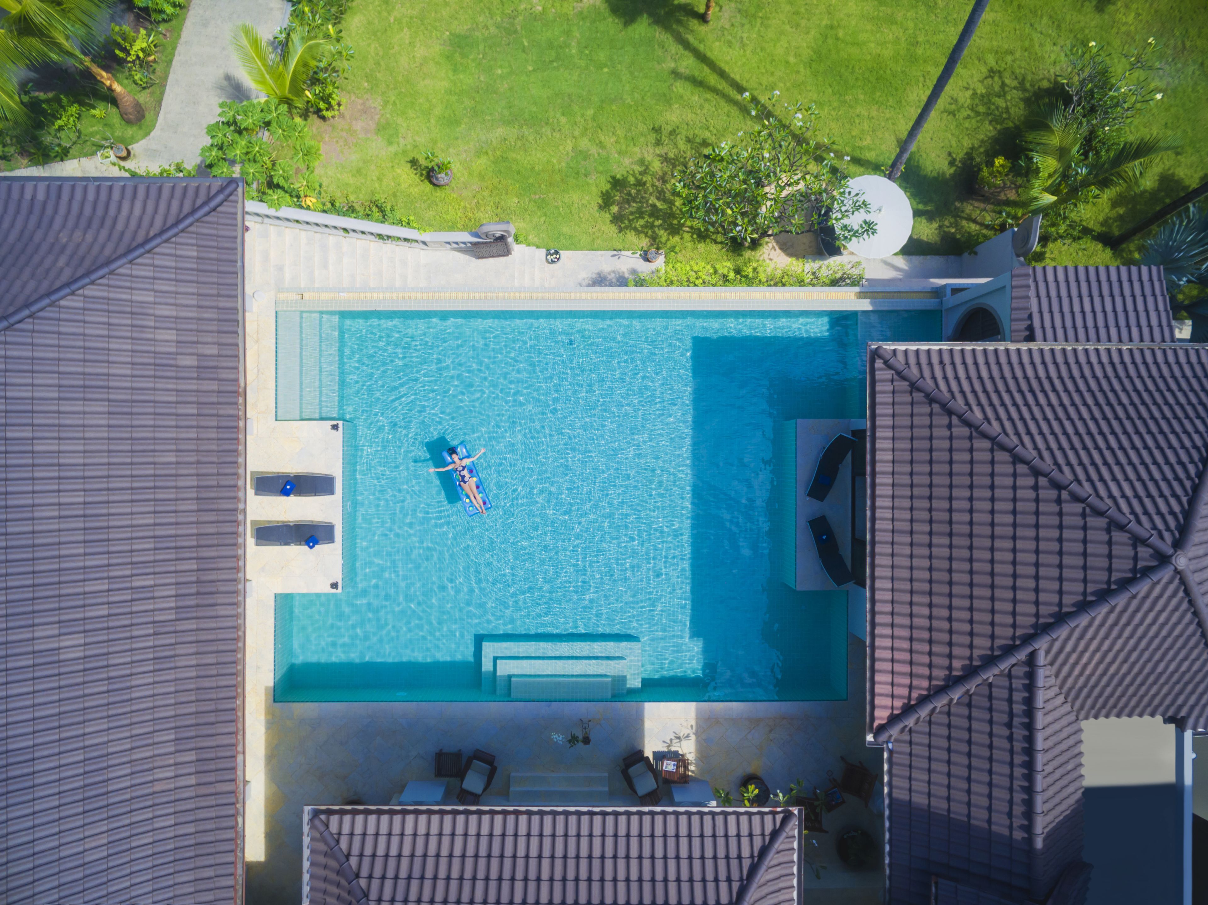 Vista aérea de uma piscina com área de estar, incluindo espreguiçadeiras e uma pequena mesa.