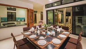 A dining area with a rectangular table set for four, surrounded by chairs. - Luxury Beach Front Noble House Villa (Wichit)