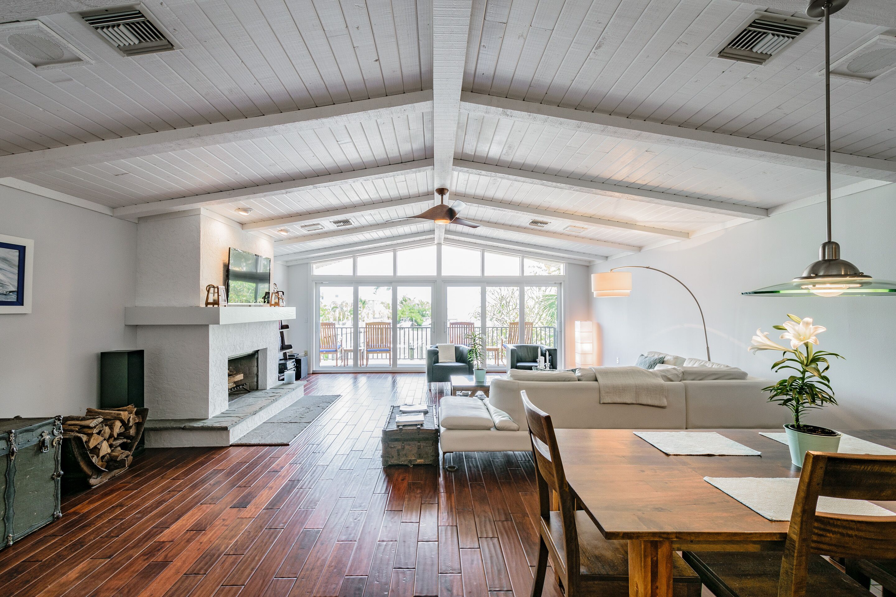 Un vaste salon doté d’un haut plafond, d’un plancher en bois, d’une cheminée, d’un canapé, d’une table à manger et d’une grande fenêtre offrant une vue sur l’extérieur.