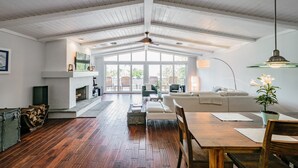 Un vaste salon doté d’un haut plafond, d’un plancher en bois, d’une cheminée, d’un canapé, d’une table à manger et d’une grande fenêtre offrant une vue sur l’extérieur.