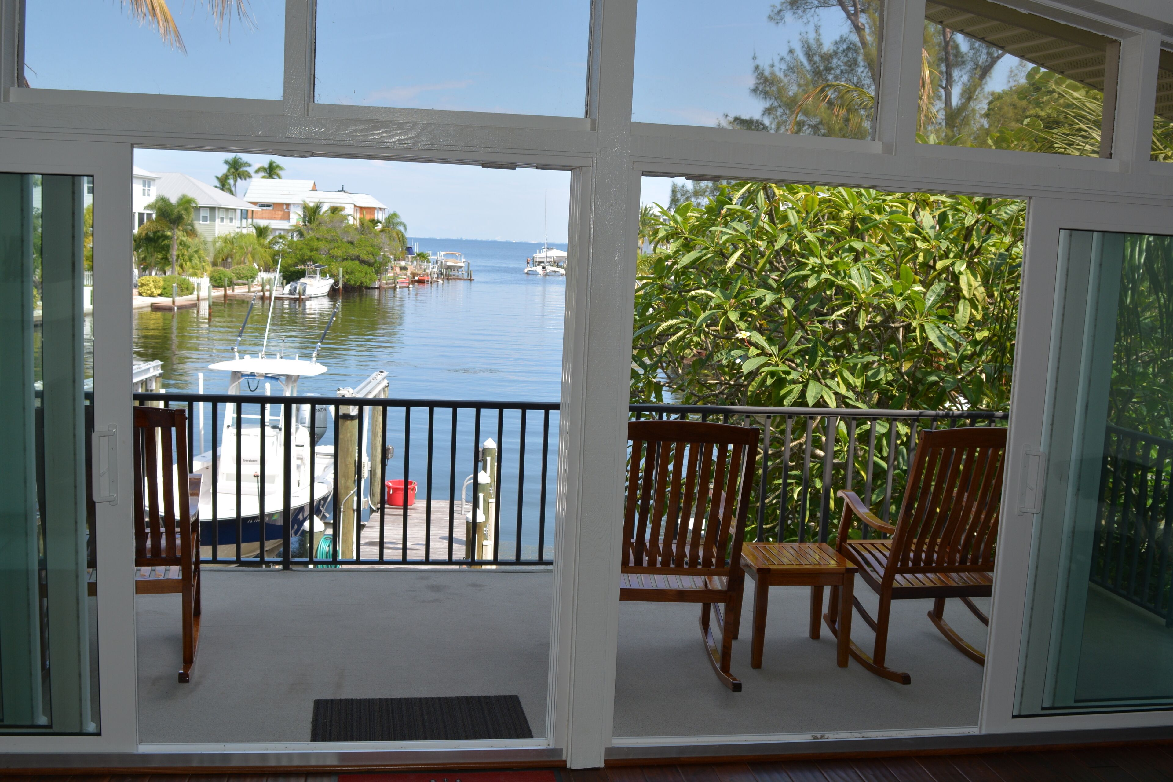 A balcony with a view of a marina, wooden chairs, and a table.