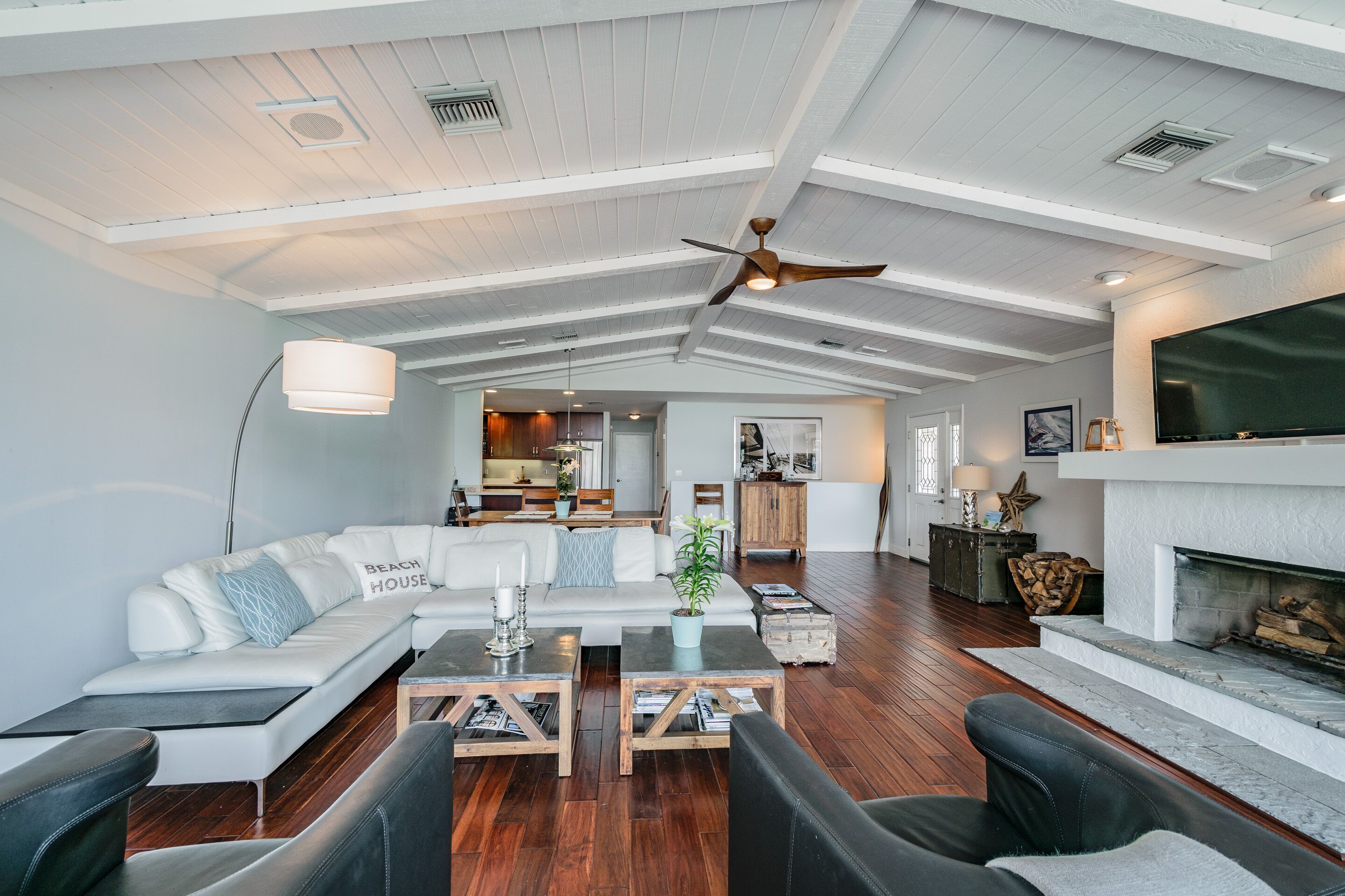 A spacious living room with a high ceiling, a fireplace, and a kitchen in the background.