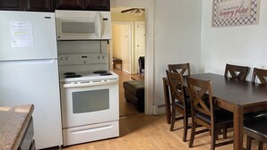 Uma cozinha equipada com geladeira, micro-ondas, fogão e forno. Há uma mesa de jantar com cadeiras e uma placa na parede.