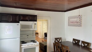 Uma cozinha com geladeira, fogão e micro-ondas brancos, armários de madeira e uma mesa de jantar com cadeiras.