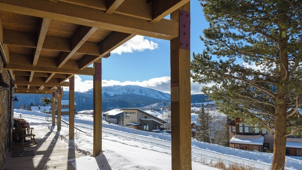 A wooden covered porch with a view of a snowy mountain landscape and a building in the background.