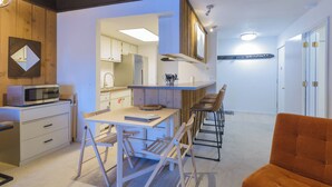 A compact kitchen with a microwave, wooden cabinets, and a bar area with stools.