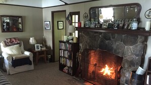 A cozy living room with a stone fireplace, a comfortable armchair, a bookshelf, and a mirror on the wall. - Lake front cottage with "million dollar" view, close to Bethel Woods (Smallwood)