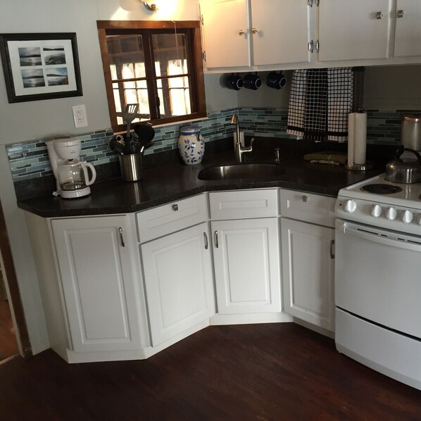A kitchen with white cabinets, a black countertop, a stove, a coffee maker, and a window with a view of the outdoors.