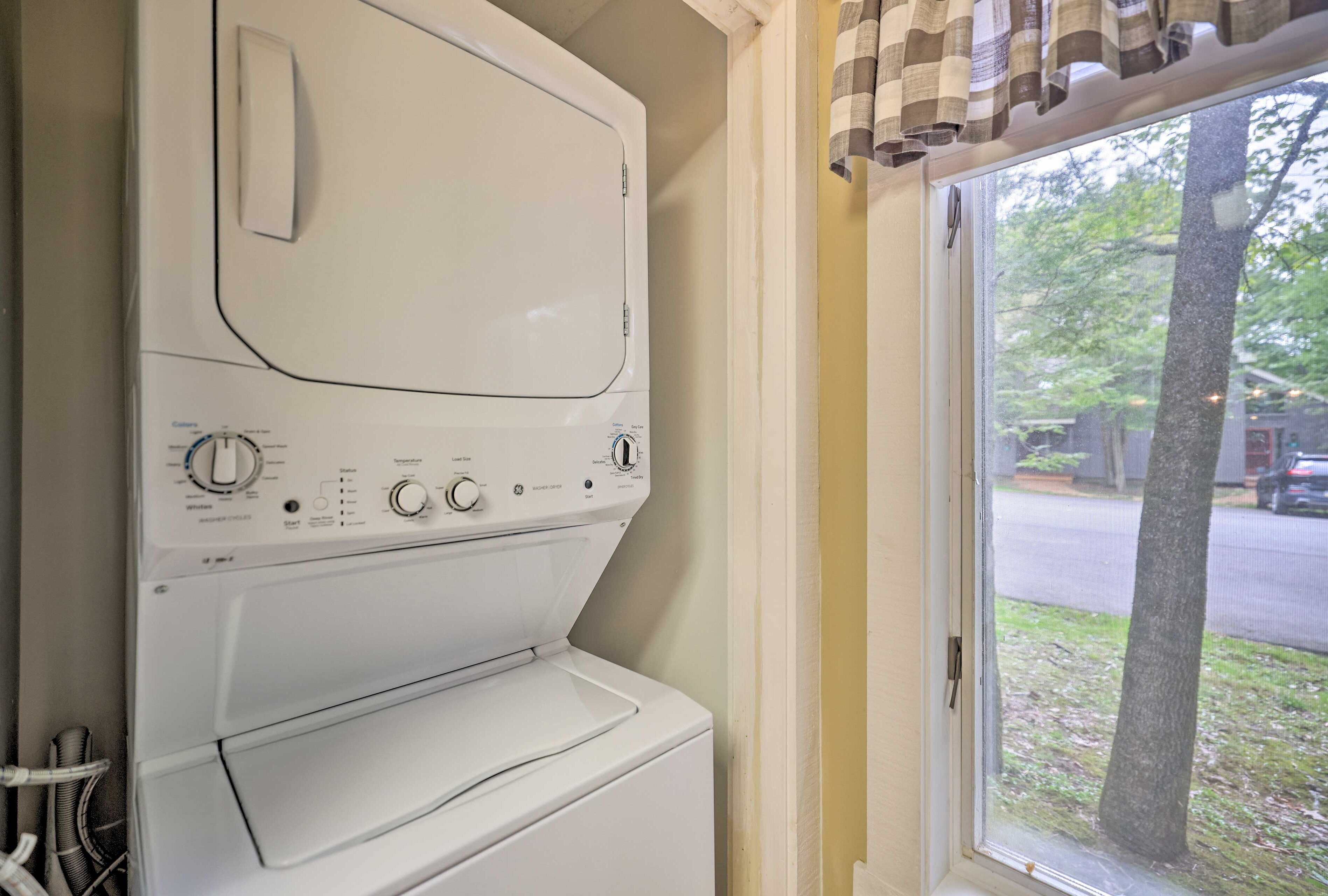 Un appareil combiné lave-linge et sèche-linge à chargement frontal, doté de boutons de commande et d’un écran numérique, placé à côté d’une fenêtre donnant sur un arbre et une rue.