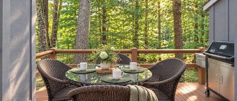 A deck with a round glass table, wicker chairs, and a grill.