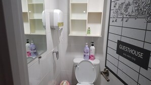 A bathroom with a toilet, hand dryer, and shelves with toiletries. - Friends of Loft - Hostel (Tongyeong)