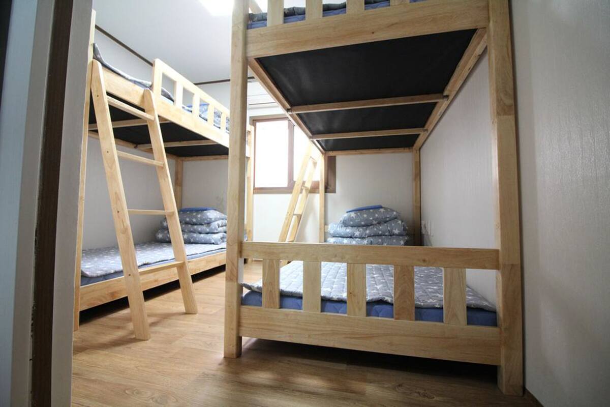 A room with bunk beds, wooden flooring, and a window.
