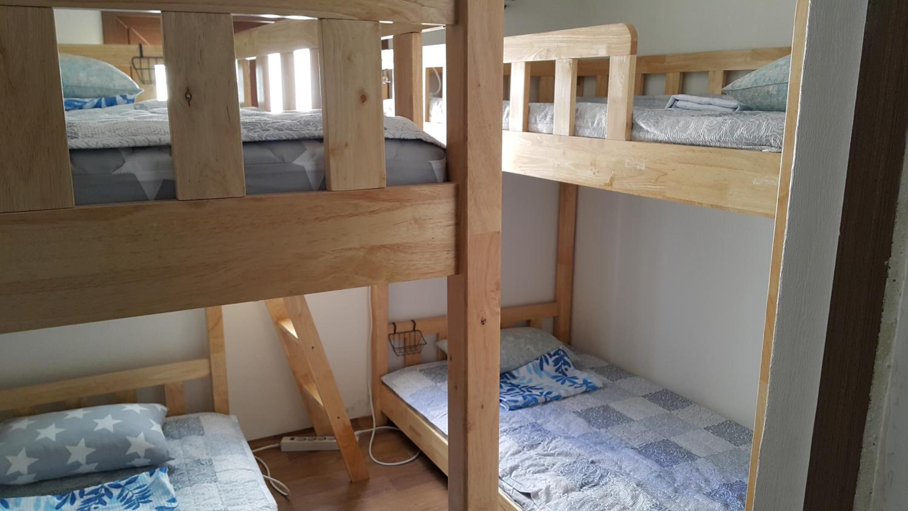 Habitación con literas de madera, una litera inferior con una manta estampada y una litera superior con una manta lisa.