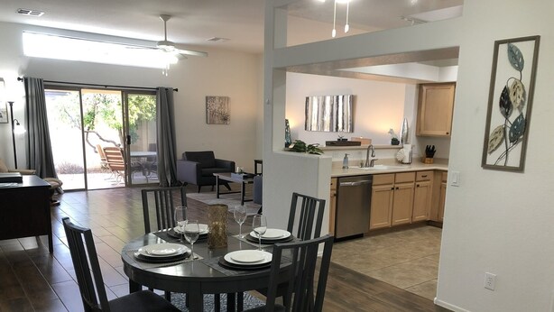 A dining area with a round table set for four, a kitchen in the background, and a sliding glass door leading to an outdoor area. - One Story w/Htd Comm Pool & Spa: GOLF & Trails Nearby, Walk to Dine & Shop, Indoor Shuffleboard (Mesa)
