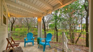 A covered porch with two blue Adirondack chairs, a wooden table with a decorative item, and a view of a garden with trees and a fence. - Minutes to it all! Restaurants, Parks, Trails. Pet's Ok (Austin)