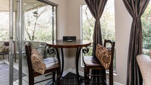 A corner room with a round table and two chairs, a glass partition, and a view of greenery outside. - Minutes to it all! Restaurants, Parks, Trails. Pet's Ok (Austin)