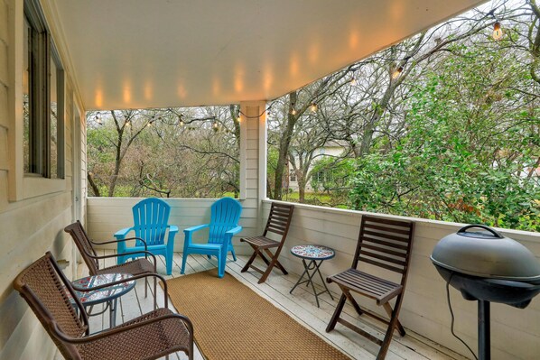 A covered porch with outdoor seating, including chairs and a table, and a barbecue grill.