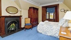 A bedroom with a fireplace, a large wooden wardrobe, a bed with a floral bedspread, and a window with a view of trees. - 2 bedroom accommodation in Dess, Aboyne (Dess, Aboyne)