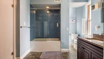 A modern bathroom with a glass-enclosed shower, a bathtub, and a vanity with a sink and mirror.