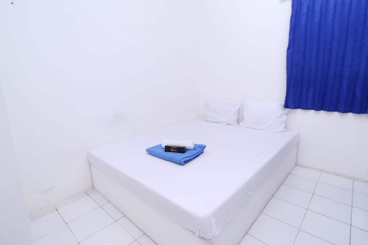 Une petite chambre propre, avec un lit simple, une serviette bleue et un petit objet posé sur le lit.