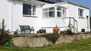 Une maison blanche avec des panneaux solaires sur le toit, un banc vert et des plantes en pot.