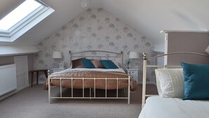 Une chambre avec un plafond en pente, un lit avec une tête de lit blanche, une table de chevet avec une lampe et une fenêtre.