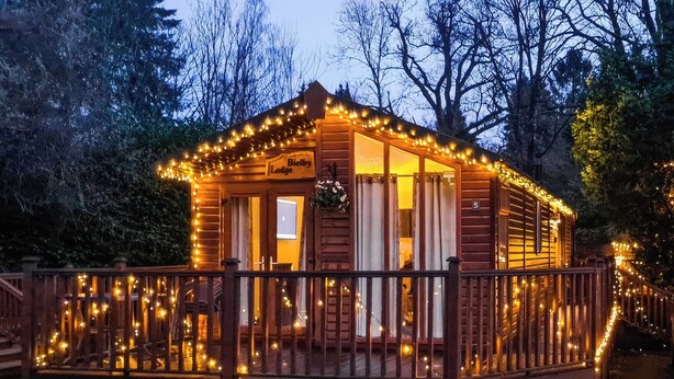 Una cabaña de madera con porche, rodeada de árboles y decorada con luces colgantes.