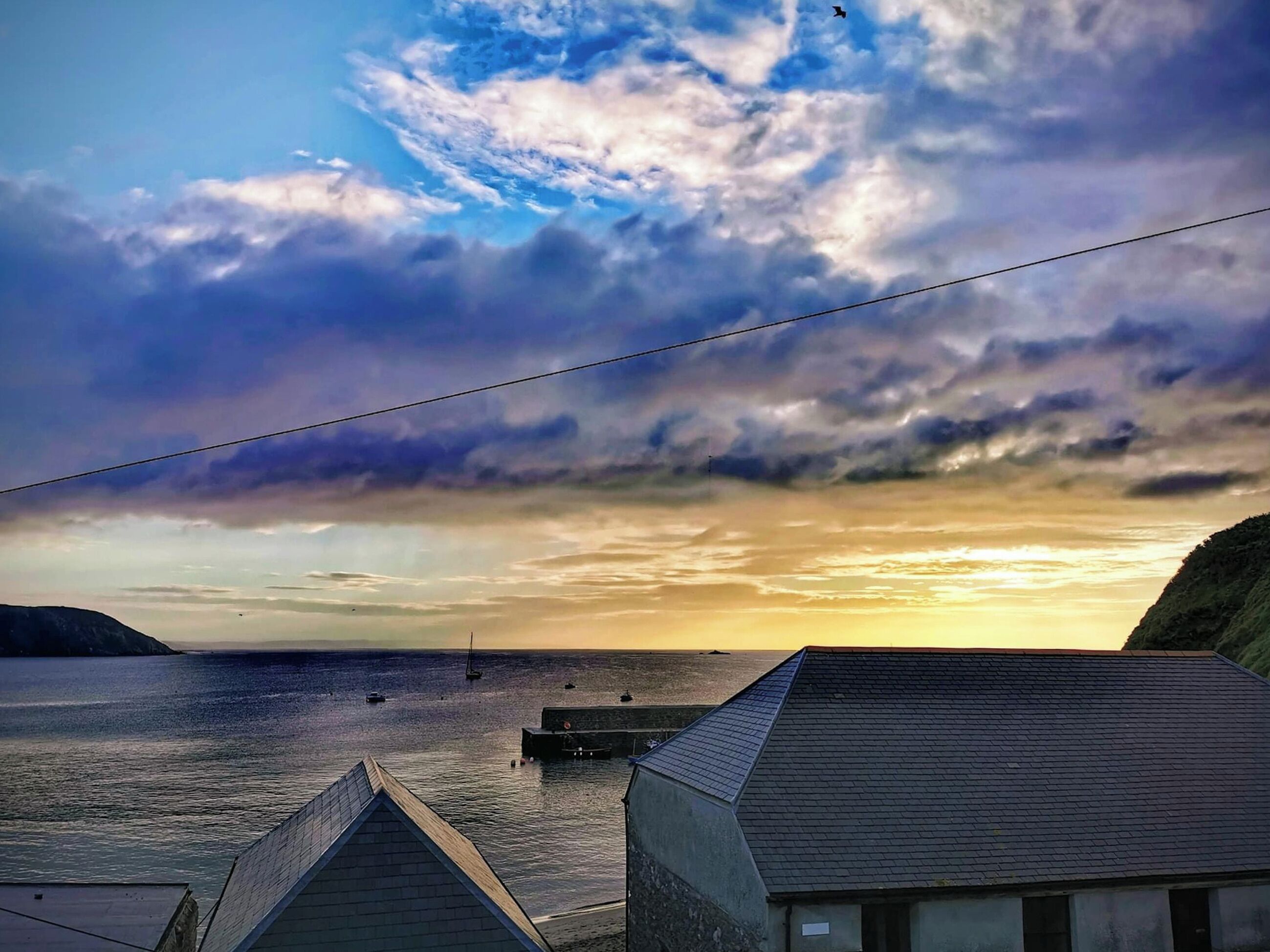 Escena costera con atardecer, barcos y muelle.