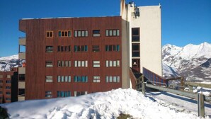 Un immeuble à plusieurs étages, doté d’une façade en bois et de nombreuses fenêtres, se dressant sur fond de montagnes enneigées.