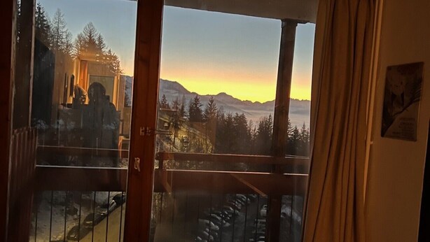 Une pièce dotée d’une grande fenêtre donnant sur un paysage montagneux au coucher du soleil.